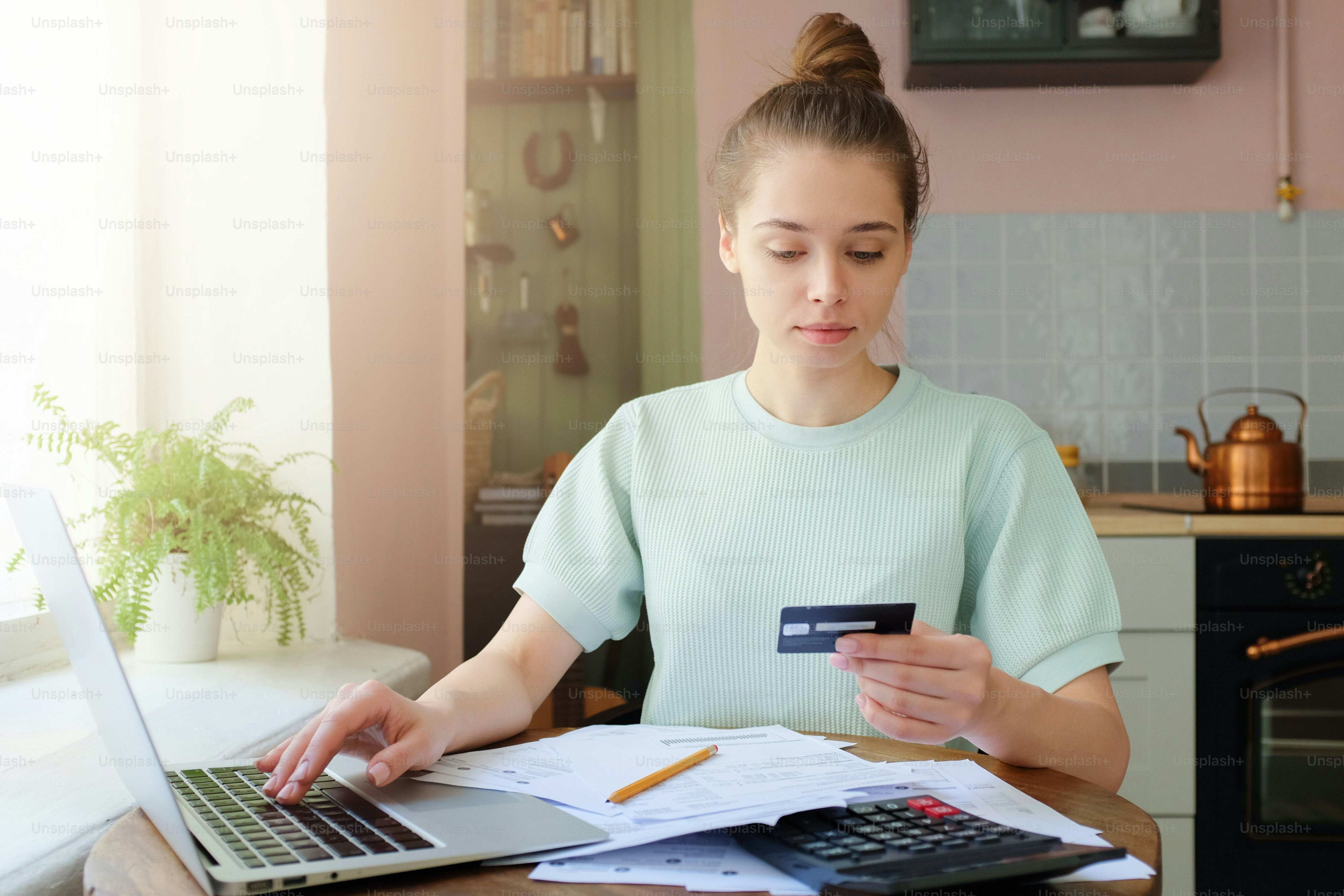 A woman using a laptop and credit card at a table in a kitchen